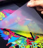 A person lifts a semi-transparent sheet to reveal a multicolored, psychedelic design featuring various abstract shapes and vibrant colors